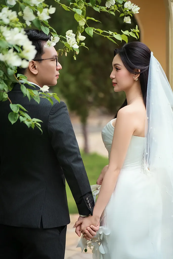 Chú rể và cô dâu nắm tay dưới giàn hoa